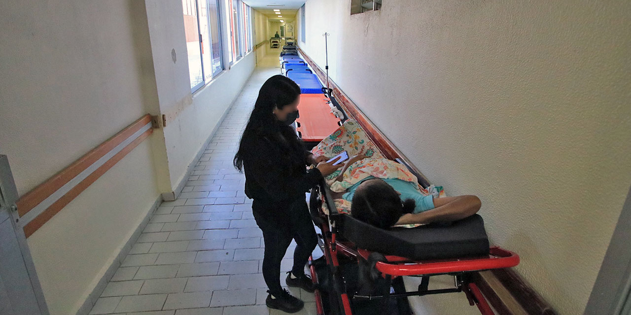 Foto: Adrián Gaytán // En la penumbra y en un pasillo del hospital, una mujer monta guardia de pie con un familiar en camilla.
