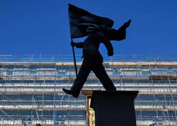 La estatua es de un hombre con traje marchando, con una pierna fuera del pedestal, mientras sostiene una bandera que le cubre el rostro.